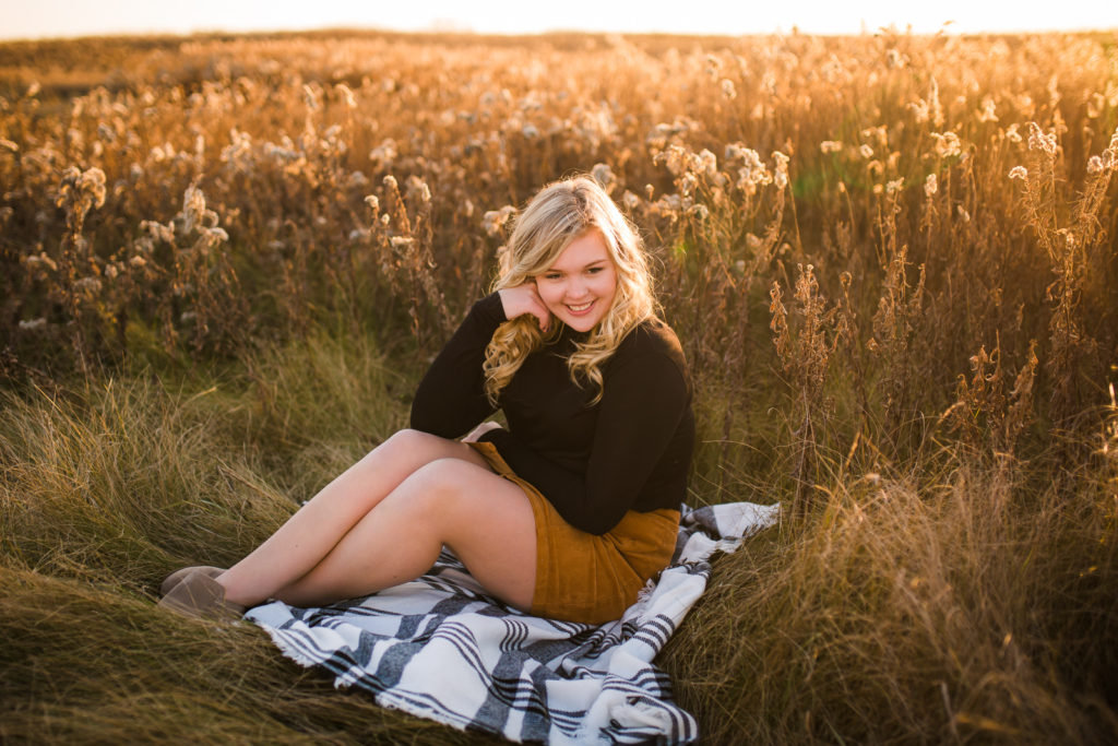 Girl sitting on a blanket in a golden field at sunset