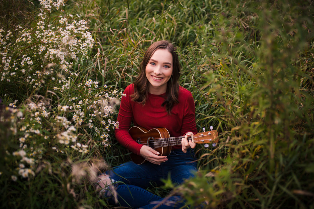 Girl sitting in wildflower field playing ukulele