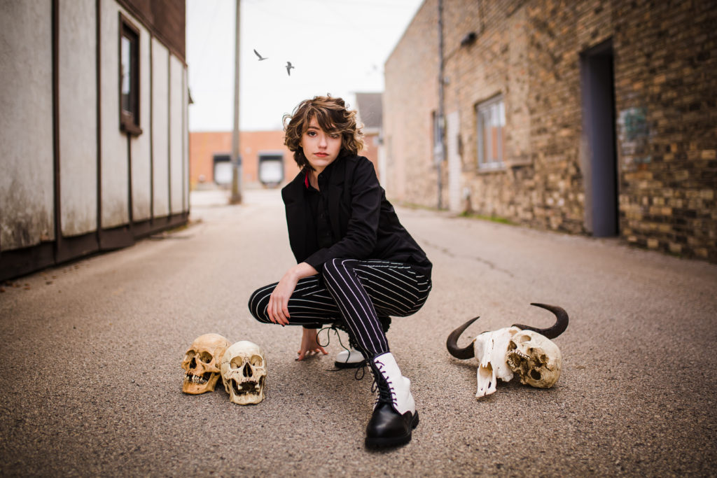 Girl posing in an alley with skulls and birds flying overhead